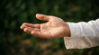 © Udin - A person's hand is extended outward in a gesture of peace or greeting outdoors.