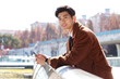 © DaoYenThu - Smiling young businessman using smartphone and earphones outdoors in the city