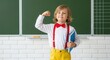 © Vector KIng - Young boy in white shirt, red bowtie, and yellow trousers flexing arm in front of chalkboard