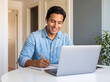 © Kin-Studio - Smiling young man working efficiently from home with his laptop and notebook, wearing wireless earbuds.