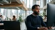 © Eve - Focused young Black male software engineer analyzing computer code on desktop monitor screen while working at modern digital technology agency corporate open space office studio.