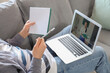 © Pixel-Shot - Male student with notebook and laptop studying online on sofa at home, closeup