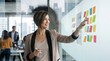 © Eve - Creative female project manager pointing at colorful sticky notes on glass wall brainstorming lean marketing strategy with blurred colleagues in modern corporate office workspace photo asset
