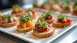© Trushchenko_O - Assorted canapes featuring toasted bread topped with colorful cherry tomatoes and fresh herbs arranged on a white platter in a modern dining setting