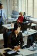 © DragonImages - Vertical shot of Asian young adult woman working in call center office, wearing headset and taking notes at computer. Useful for customer support, team communication, service business