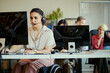 © DragonImages - Young adult woman with disability working in call center, wearing headset and using computer in team office. Customer support and inclusive workplace concept for service business marketing