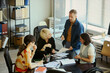 © DragonImages - High angle view of diverse young adult team collaborating in office, reviewing documents and planning strategy. Ideal for business teamwork, inclusion, leadership, workplace communication