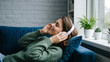 © warut_____z - Beautiful young woman listening to music with headphones while relaxing on sofa at home.