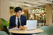 © Stella 16 - Young Asian Businessman Working on Laptop and Taking Notes in Modern Coworking Cafe Space
