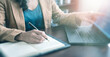 © mocklyn - A close-up of a person writing in a notebook while using a laptop. The scene captures a workspace, reflecting productivity and organization in a modern setting.