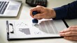 © James - Close up hand stamping approval checkmark on contract document with charts, business agreement signature process in office workspace with laptop background