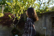 © SHOTPRIME STUDIO - Candid woman in plaid shirt walks through a sunlit garden, capturing a simple lifestyle moment with calm, reflective mood and natural surroundings
