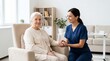 © Iuliia - Young nurse holding hand of elderly woman sitting in armchair. Caregiver providing professional assistance and support at home. Healthcare service, retirement and compassion concept.