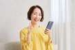 © siro46 - リビングでスマートフォンを持つ女性　グッドサイン