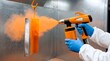 © Razia - Industrial worker in protective gear using orange powder coating spray gun on metal plate in factory