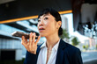 © Davor - Businesswoman using smartphone voice assistant outdoors downtown