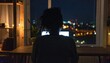 © ahmat - Silhouette of a person working on a laptop at night with city lights in the background.