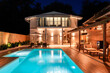© Maria - Luxury modern house with illuminated swimming pool and outdoor lounge area at night. Elegant backyard featuring wooden deck and cozy lighting