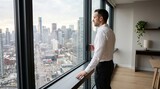 Businessman standing by floor-to-ceiling window overlooking city skyline with coffee cup