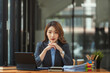 © Songsak C - Portrait of serious Asian businesswoman with hands under chin looking at camera at office desk.