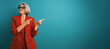 © DMegias - Senior businesswoman in a red suit and glasses pointing right, confidently presenting or indicating an area for text or product
