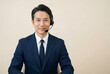 © TMGM - オフィスでヘッドセットを装着し笑顔でカメラを見る紺色スーツの40代日本人男性