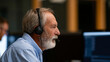 © Kateryna Arkhypova - Anonymous bearded senior technical support specialist talking on a headset while working on a computer in a monitoring room with display screens, faceless, defocused, with copy