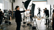 © Anindra - A photographer directing a model during a photoshoot in a studio with lighting equipment, reflectors, and beauty products on a table