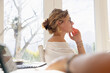 © Marc Romanelli - young woman at table, using mobile phone and thinking