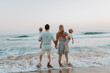 © Halfpoint - A family with two toddler children walking on beach on summer holiday at sunset.