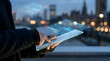 © fitria - A person's hands interact with a futuristic transparent digital tablet displaying glowing holographic data and user interfaces against a blurred city night background.