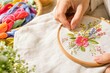 © Studio - Female hands embroidering vibrant floral pattern on linen fabric in wooden hoop, close-up of creative handmade craft hobby in cozy home workshop with warm natural light