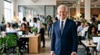 © horizon - Cheerful senior professional man wearing a sharp tailored navy blue business suit smiles warmly while standing in a bustling modern office.