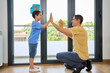 © cunaplus - Happy mixed race father and son giving each other a high five while cleaning at home. Little hispanic boy helping his dad wash windows. Parent and child joining hands to celebrate achievement at home