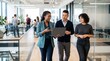 © Eve - Diverse group of young professionals walking through a modern office, engaged in a discussion while holding a laptop. Corporate culture, teamwork, modern workplace, collaboration, business.