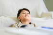 © Kornkanok - Tired Asian preteen boy resting his head on a comfortable sofa after finishing homework. Representing study breaks, childhood relaxation, daydreaming, and domestic learning routines