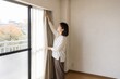 © AiPhoto - 秋の内見で女性がカーテンを開ける賃貸物件