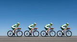 Four professional cyclists in green and white team kit riding in a pace line against blue sky
