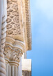 © Patricia Hikari - Close-up of an elegant ornamental stone column and cornice ceiling with intricate carved patterns and details against a clear blue sky.