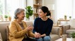 © Xenia - Elderly mother and adult daughter talking on a sofa. Senior woman holding hands with a younger female caregiver in a living room. Family bonding and support concept