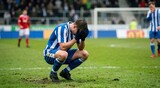 Devastated soccer player crouching on pitch with head in hands after missing shot. Emotional football athlete reacting to defeat during match