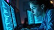 © Vadym - Woman coder works on computer screen in dark room. Multiple monitors display code. Blue light illuminates her face. She is focused on programming task.