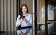© matinee - Young businesswoman smiling while using smartphone during a coffee break in a modern cafe workspace.