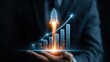 © Sikandar - Businessman holds a holographic rocket ship launching over a rising financial graph to symbolize huge growth.