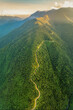 © Nguyen Phong - Breathtaking aerial view of a winding road running along the ridge of lush green mountains illuminated by golden sunrise light.
