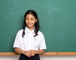 © Adkia - Shy school girl standing against blank green chalkboard for first day back to school concepts.
