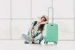 © deagreez - Sad woman leaning on suitcase in airport terminal, enjoying casual travel attire and tropical style for her journey