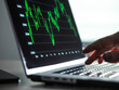 © Connect Images - Hand pointing at laptop screen displaying green financial graph in a dimly lit room.