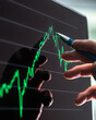 © Connect Images - Hand holding a pen pointing at a green financial chart on a screen.
