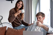 © luciano - Young couple enjoying coffee and leisure time at home, a woman sitting on the sofa armrest, a man using a laptop